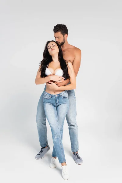 Homem muscular abraçando mulher sexy no sutiã branco no cinza — Fotografia de Stock