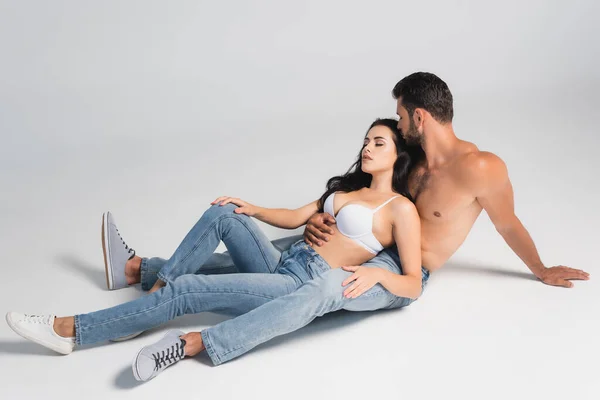 Homem sem camisa em jeans e mulher em sutiã deitado em cinza — Fotografia de Stock