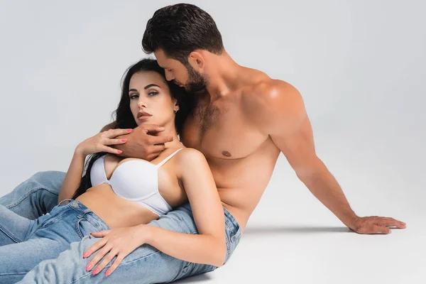 Homme musclé en jeans denim étreignant femme en soutien-gorge couché sur gris — Stock Photo