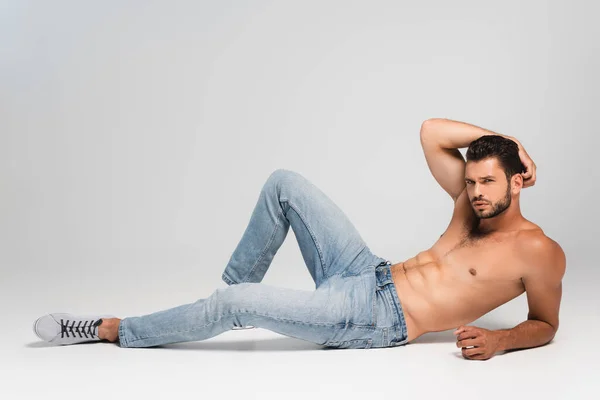 Hombre musculoso y barbudo en jeans azules acostado sobre gris - foto de stock