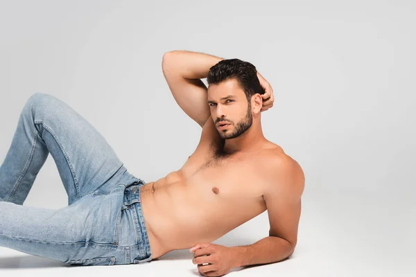 Sexy and bearded man in denim jeans lying on grey — Stock Photo