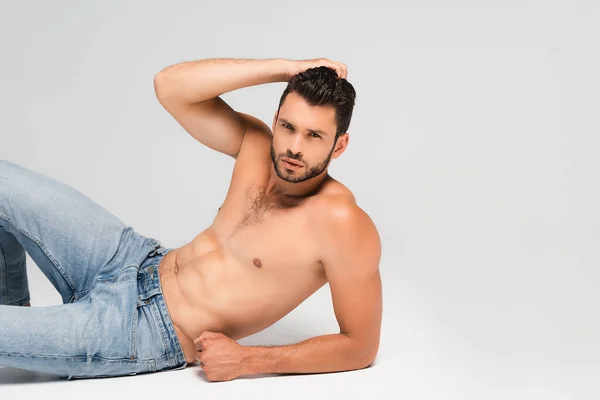 Мужчина без рубашки и бороды в джинсах, лежащих на сером — стоковое фото