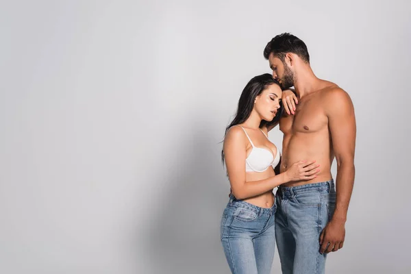 Спокуслива жінка в бюстгальтері, торкаючись м'язистого чоловіка, що стоїть на сірому — стокове фото
