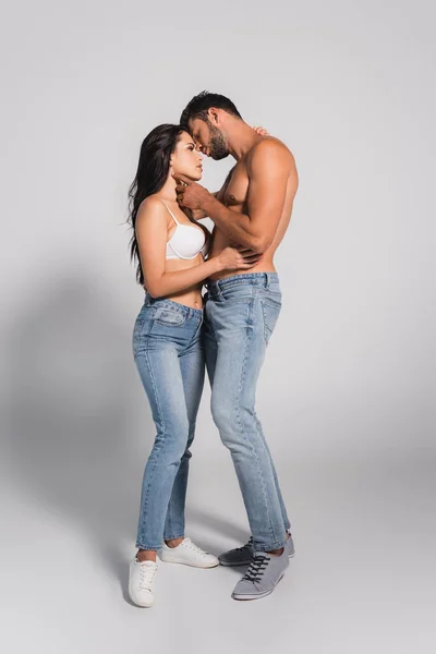 Muscular man standing and touching seductive woman in bra on grey — Stock Photo