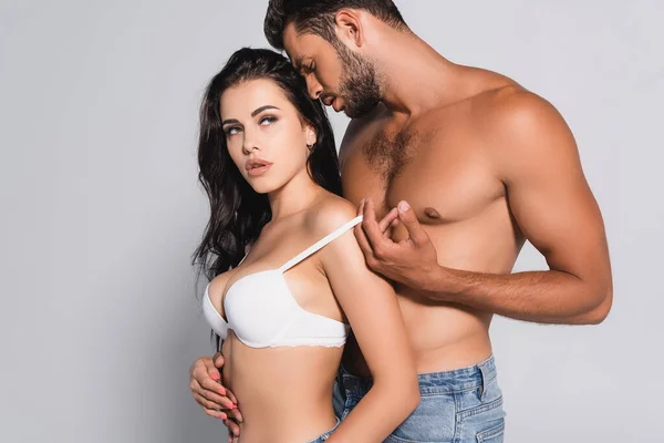 Muscular man standing and undressing seductive woman in bra on grey — Stock Photo