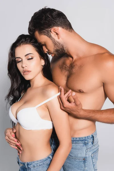 Senza maglietta uomo in piedi e spogliarsi seducente donna in reggiseno isolato su grigio — Foto stock