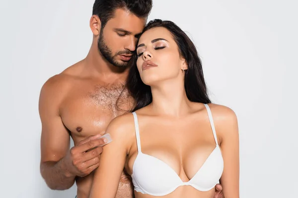 Uomo senza maglietta tenendo cubetto di ghiaccio vicino donna sexy in reggiseno isolato su bianco — Foto stock