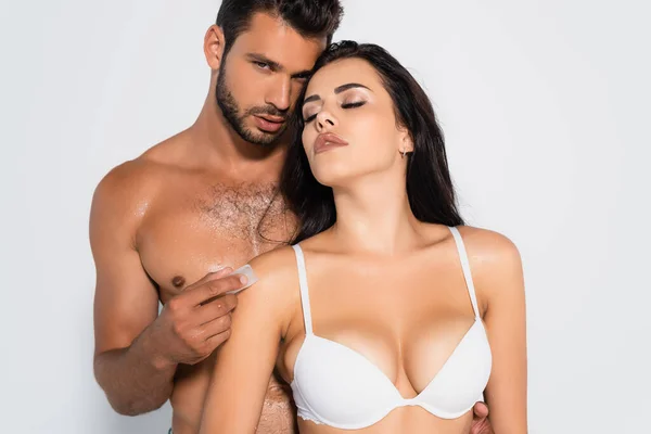 Senza maglietta uomo tenendo congelato ghiaccio cubo vicino sexy donna in reggiseno isolato su bianco — Foto stock