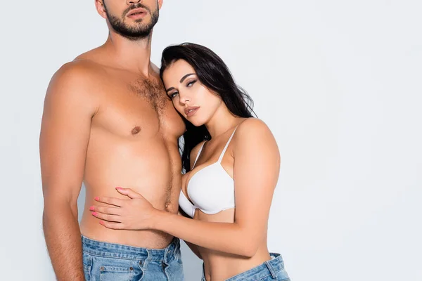 Morena mujer en sujetador abrazando musculoso y barbudo hombre aislado en blanco - foto de stock