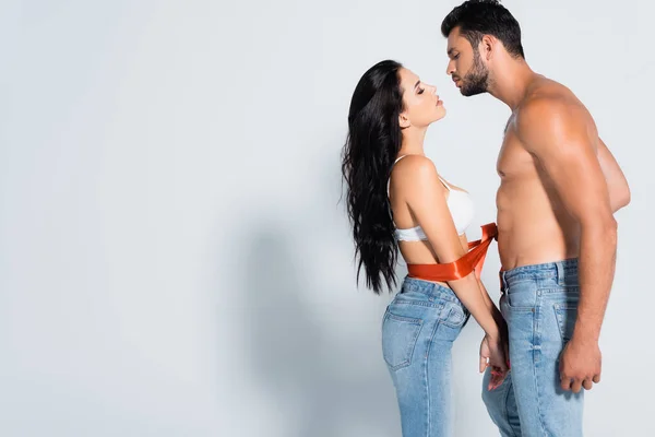 Profilo uomo muscoloso e barbuto legatura donna sexy in reggiseno e jeans su bianco — Foto stock
