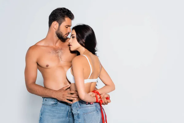 Morena e submissa mulher com as mãos amarradas perto de homem muscular isolado no branco — Fotografia de Stock