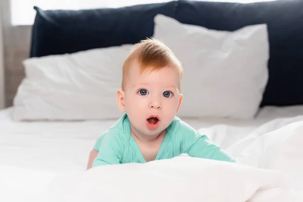 Selektive Fokussierung des Säuglings, der mit offenem Mund in die Kamera schaut, während er im Bett krabbelt — Stockfoto