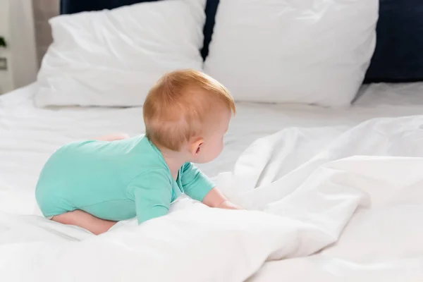Selektiver Fokus des Säuglings im Babystrampler, der im Bett krabbelt — Stockfoto
