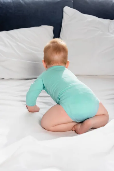 Visão traseira da criança infantil no bebê romper rastejando na cama — Fotografia de Stock