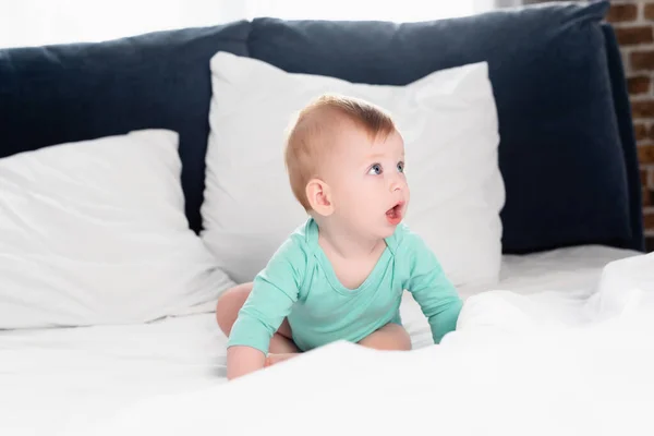 Infant boy in baby romper crawling in bed with open mouth — Stock Photo