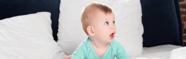 Récolte panoramique de bébé garçon regardant loin tout en rampant dans le lit avec la bouche ouverte — Photo de stock