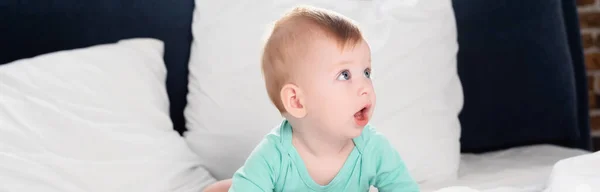 Panoramic crop of infant boy looking away while crawling in bed with open mouth — Stock Photo