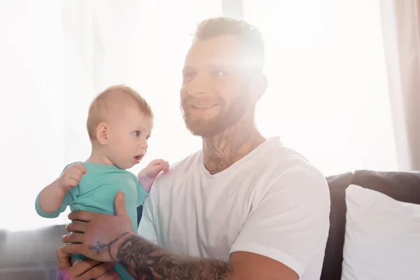 Giovane padre eccitato che tiene in braccio il bambino mentre è seduto in camera da letto — Foto stock