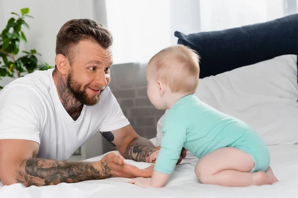 Selective focus of excited father having fun with infant son crawling on bed — Stock Photo