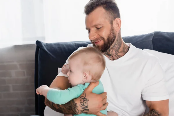 Young father in white t-shirt holding infant kid while sitting in bedroom — Stock Photo