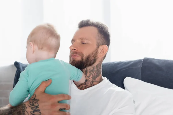 Barbuto, uomo tatuato che tiene bambino in camera da letto — Foto stock