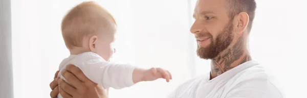 Panoramic shot of young bearded man holding baby boy in hands — Stock Photo