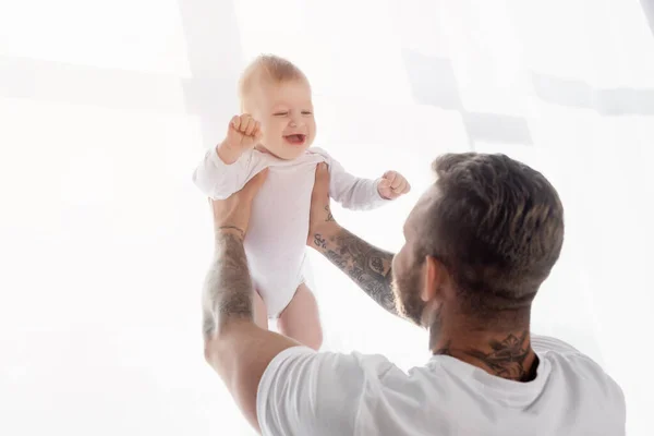 Back view of young father holding excited baby boy in outstretched hands — Stock Photo