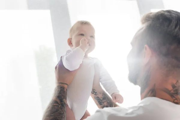 Messa a fuoco selettiva del bambino che tiene la mano in bocca nelle mani del padre contro il sole — Foto stock