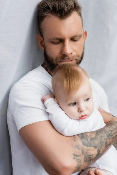 Joven barbudo hombre sosteniendo infante hijo en manos en casa - foto de stock