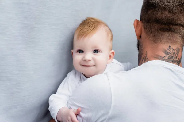 Rückansicht tätowierter Mann mit freudigem Säugling, der in die Kamera blickt — Stockfoto