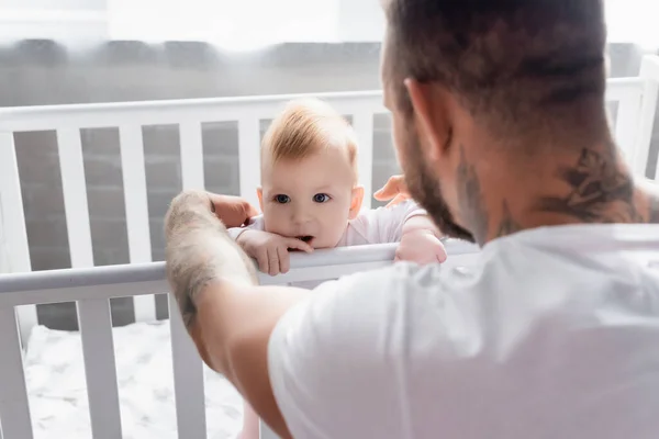 Back view of young father supporting infant son standing in crib — Stock Photo