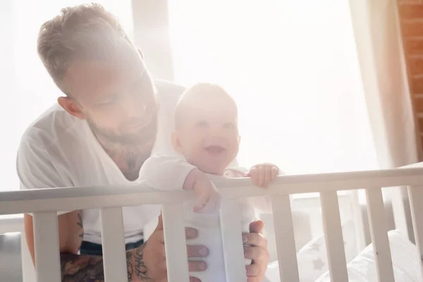 Junger bärtiger Mann stützt aufgeregten Jungen, der mit offenem Mund im Kinderbett steht — Stockfoto