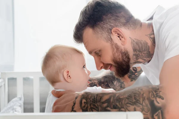 Visão lateral do jovem homem tatuado e filho bebê olhando um para o outro cara a cara — Fotografia de Stock