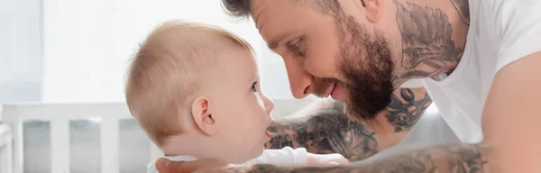 Imagen horizontal de hombre joven tatuado e hijo pequeño mirándose cara a cara - foto de stock