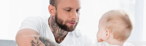 Selective focus of young tattooed man looking at infant son, panoramic shot — Stock Photo