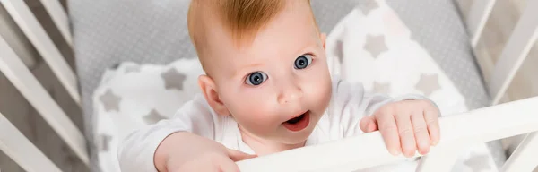 Horizontal concept of infant boy looking at camera while standing in crib — Stock Photo