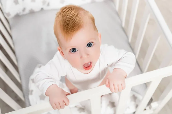 Blick von oben auf ein Kleinkind, das mit offenem Mund in die Kamera blickt, während es in der Krippe steht — Stockfoto