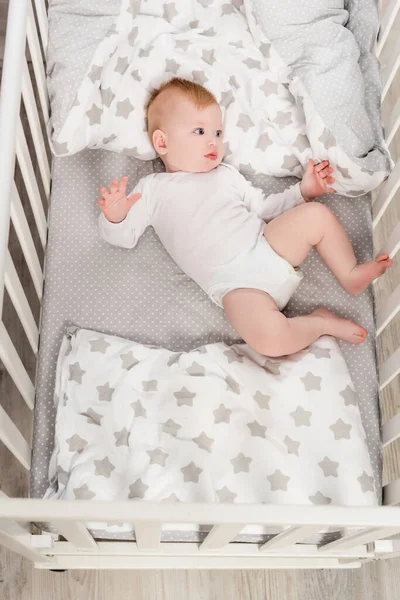 Top view of infant boy in baby romper lying in crib — Stock Photo
