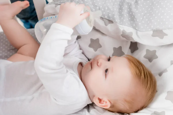 Infant boy holding baby bottle while lying in bed — Stock Photo