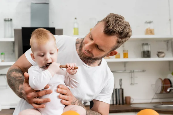 Junge leckt in Küche Löffel in der Nähe von jungem Vater — Stockfoto