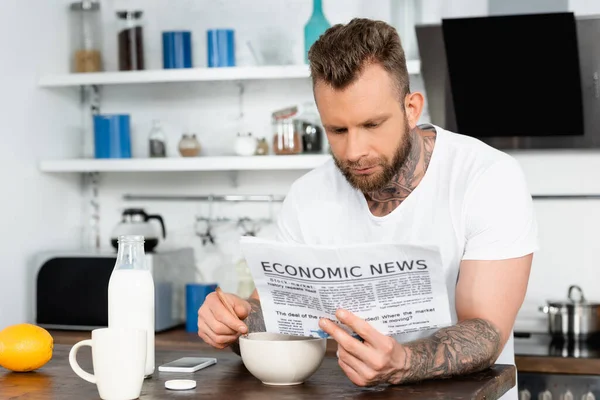 Jovem barbudo homem em branco t-shirt ler jornal durante café da manhã na cozinha — Fotografia de Stock