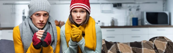 Récolte panoramique de jeunes couples dans des chapeaux chauds et gants regardant la caméra tout en gelant dans la cuisine froide — Photo de stock