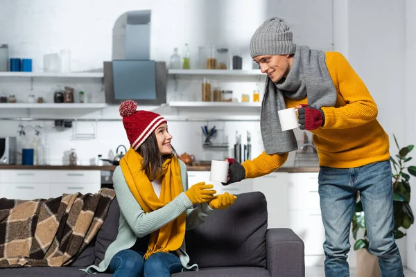 Молодой человек в вязаной шляпе и перчатках, дающий теплый чай замораживающей девушке — стоковое фото