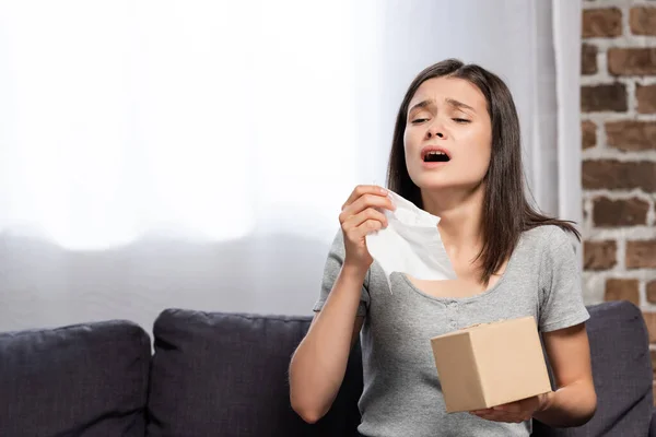 Sick young woman sneezing while holding paper napkin at home — Stock Photo