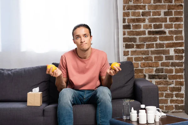 Malade tenant des citrons frais assis sur le canapé près de la table de chevet avec des médicaments — Photo de stock