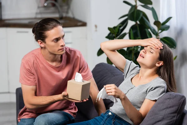 Junger Mann hält Papierservietten in der Nähe kranker Freundin mit geschlossenen Augen, die an Migräne leidet — Stockfoto