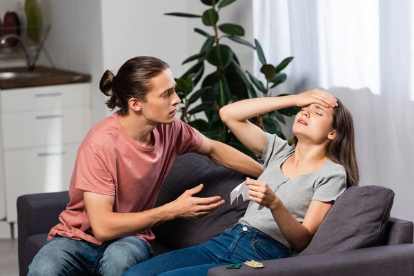 Worried man sitting near sick girlfriend touching forehead while suffering from headache — Stock Photo