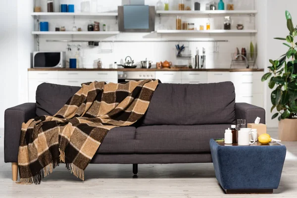 Spacious kitchen with modern furniture, plaid blanket on grey sofa, medicines and fresh lemons on bedside table — Stock Photo