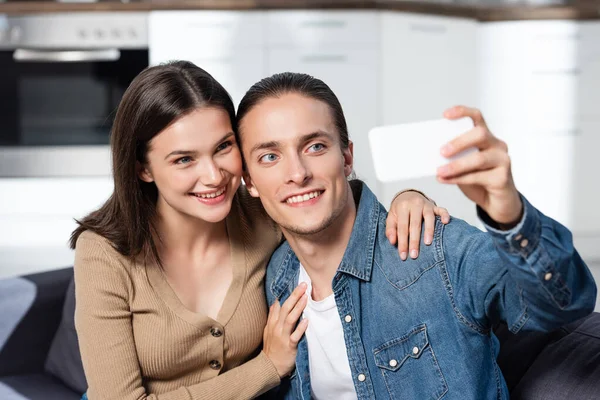 Excited woman hugging boyfriend taking selfie on smartphone at home — Stock Photo