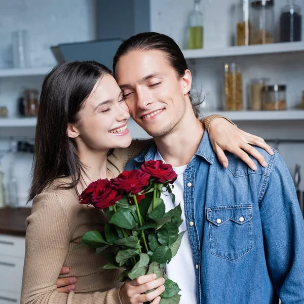 Excitée femme étreignant petit ami tout en tenant bouquet de roses avec les yeux fermés — Photo de stock